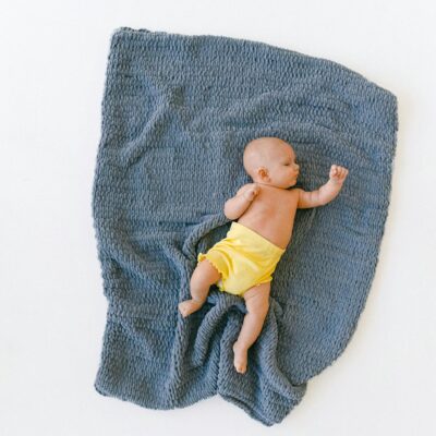 A baby peacefully sleeping on a soft, blue blanket with a yellow diaper, from an overhead view.