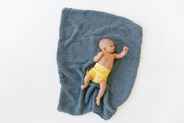 A baby peacefully sleeping on a soft, blue blanket with a yellow diaper, from an overhead view.