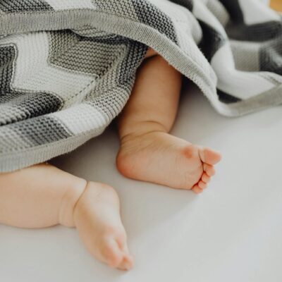 Cute baby feet peeking from under a patterned blanket, symbolizing warmth and innocence.