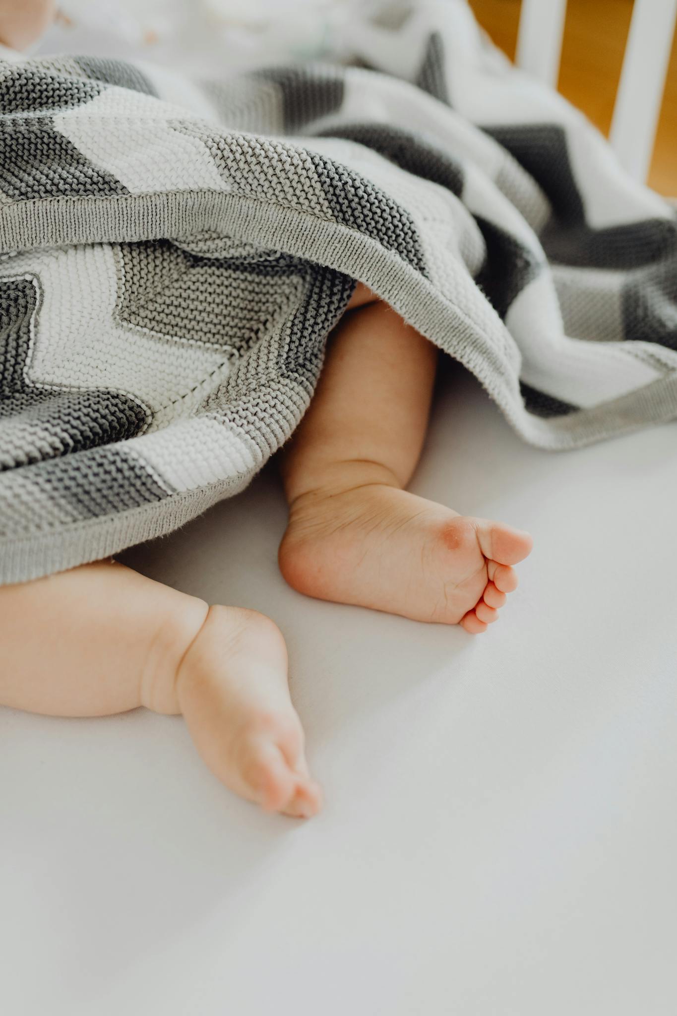 Cute baby feet peeking from under a patterned blanket, symbolizing warmth and innocence.